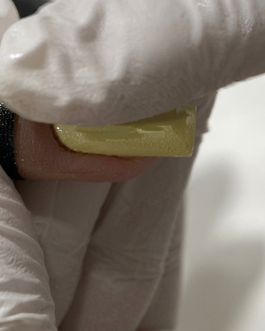 Un doigt ganté frottant de la poudre chrome perle sur un ongle jaune.