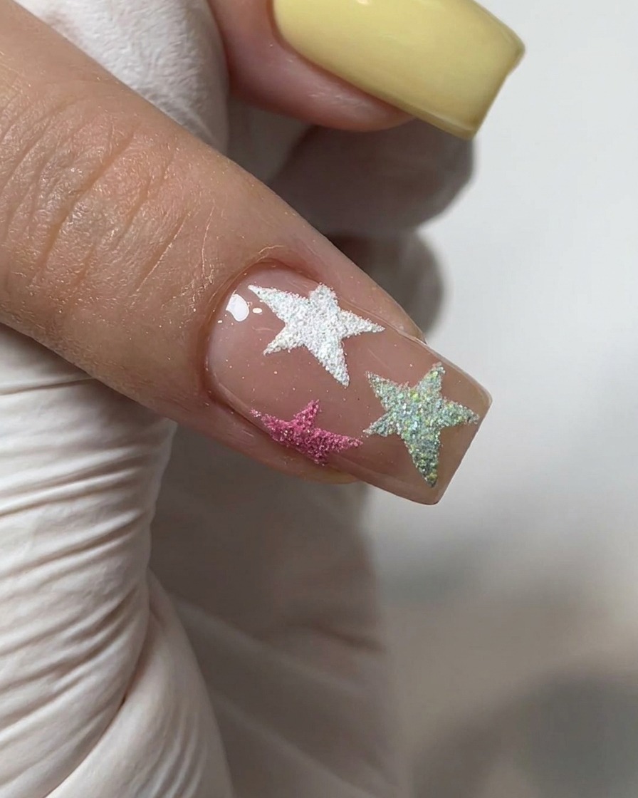 Un pinceau appliquant un top coat brillant transparent sur un ongle décoré de poudre chrome et détoiles texturées.