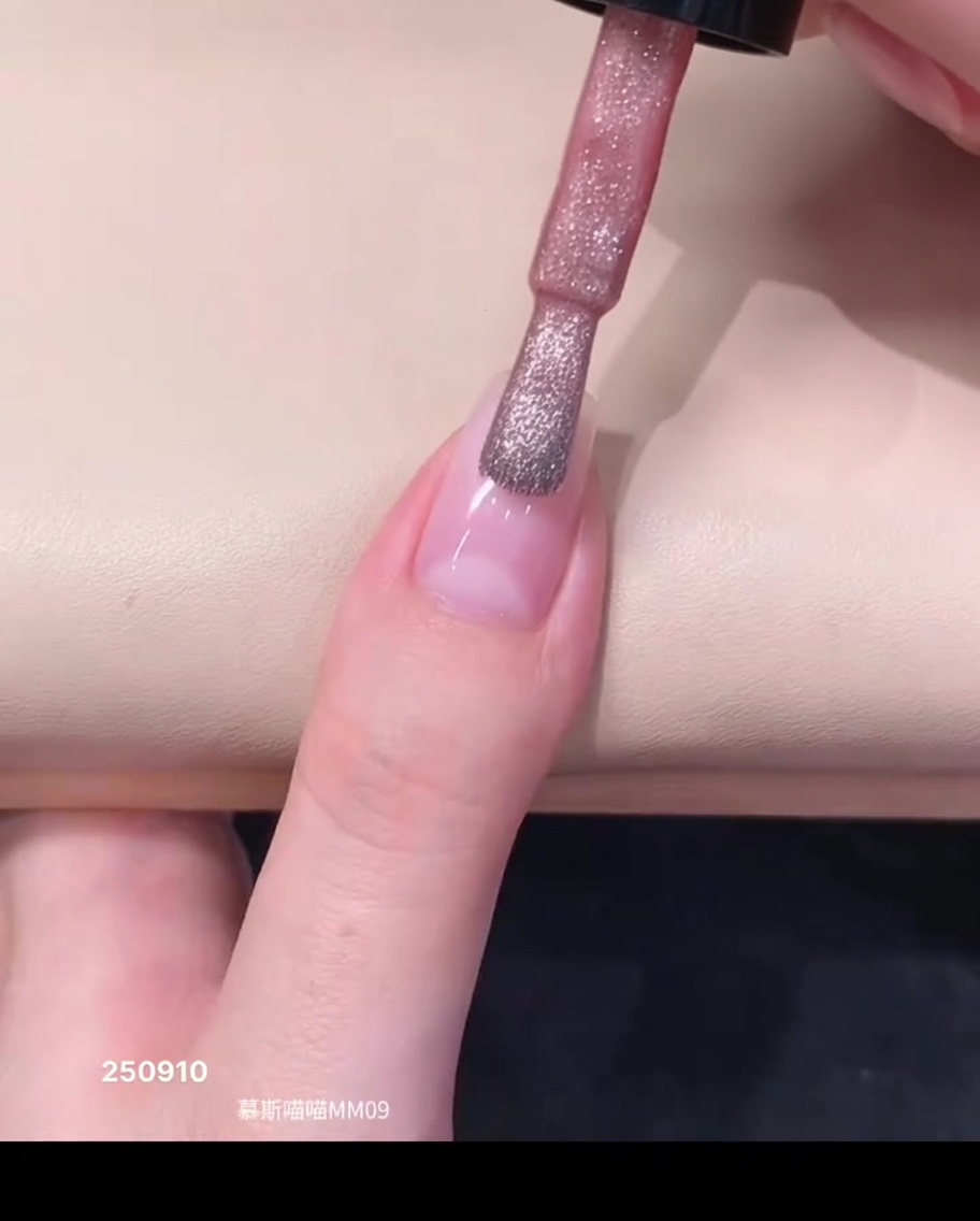 Un pinceau de vernis appliquant une goutte de vernis gel magnétique rose diaphane près de la zone des cuticules dun ongle naturel.