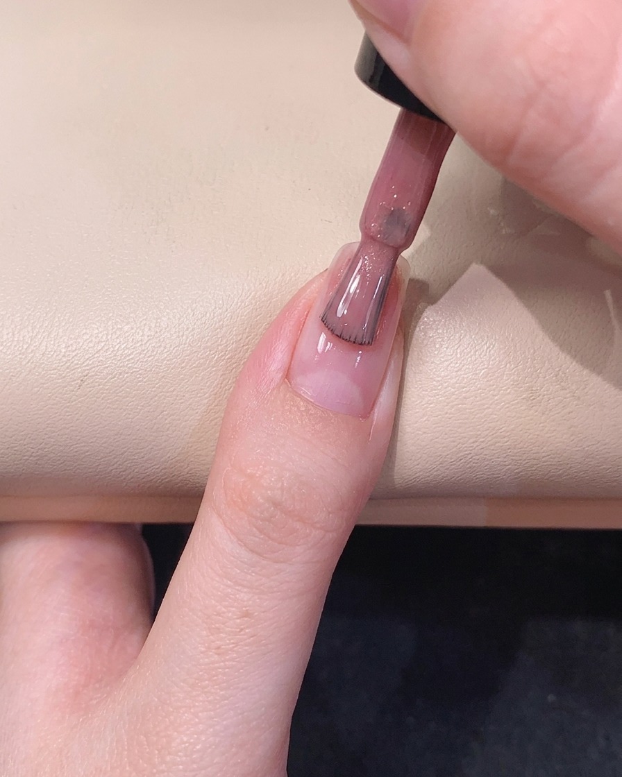 Un pinceau de vernis à ongles glissant au centre de longle, répartissant un vernis scintillant rose diaphane.