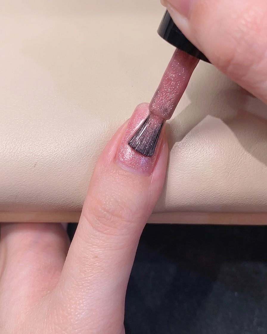 Un pinceau à ongles étalant du vernis gel magnétique rose diaphane le long du côté gauche de longle.