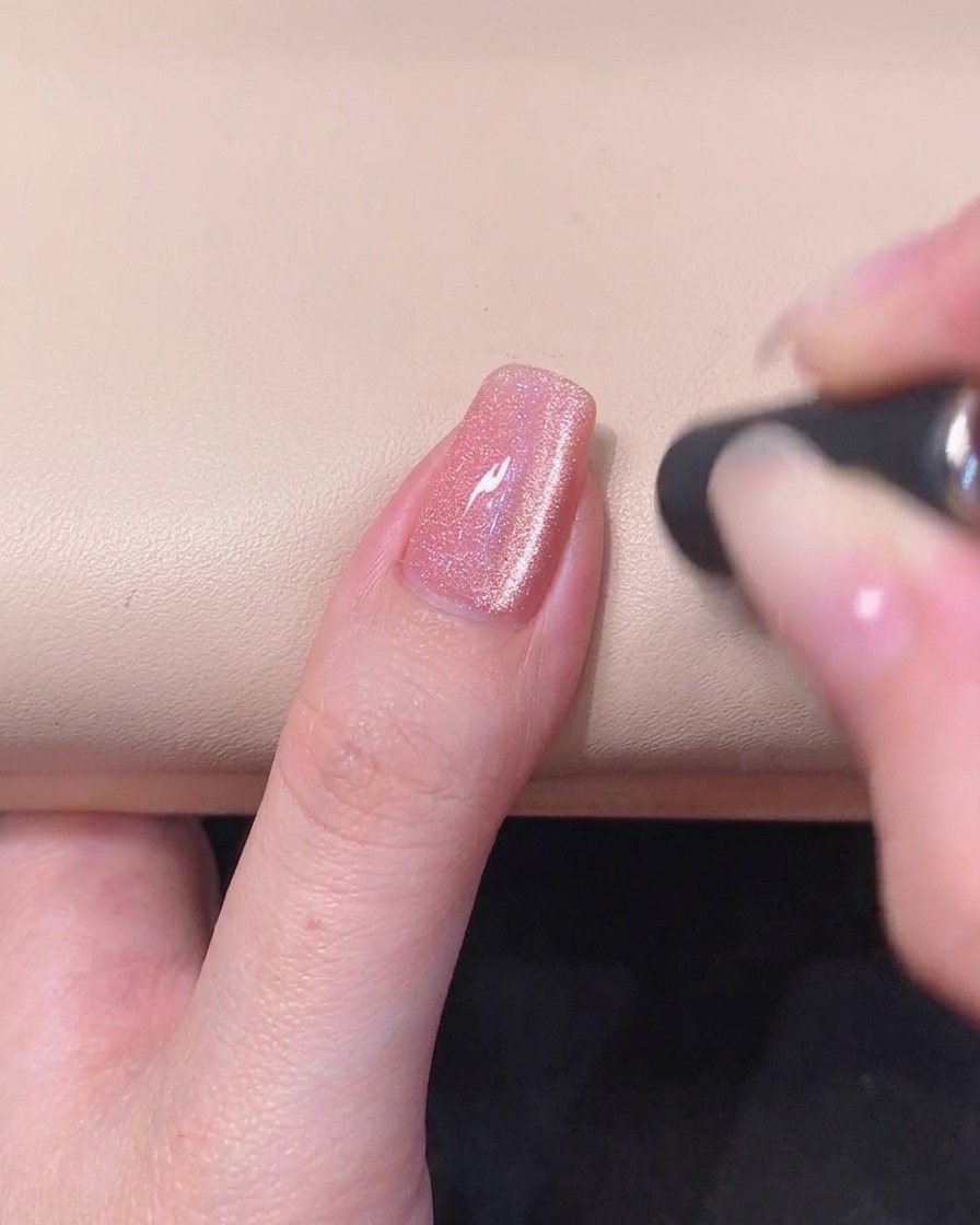 Gros plan sur un ongle en gel rose avec une strie œil-de-chat magnétique lumineuse visible à la surface du gel frais.