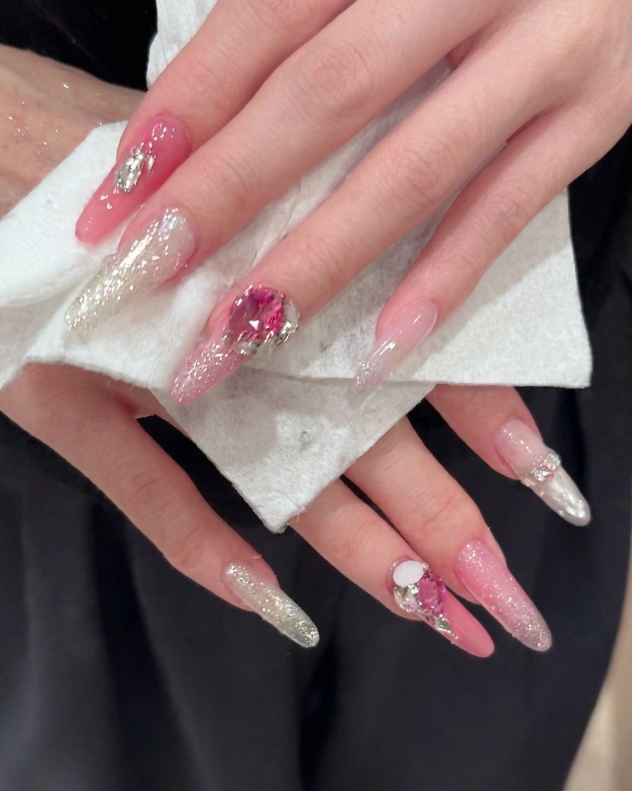 Gros plan sur des ongles longs en amande montrant les reflets détaillés des paillettes roses et argentées.