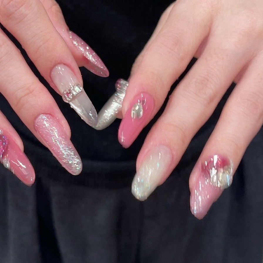 Gros plan sur des mains aux doigts écartés, révélant des ongles longs en amande roses et argentés entièrement décorés de strass scintillants.