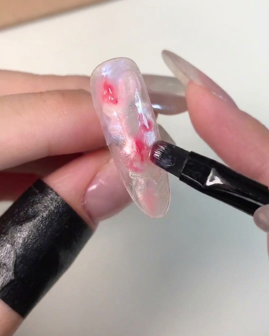 Un petit pinceau plat déposant du gel rose foncé au centre dune capsule marbrée non catalysée.