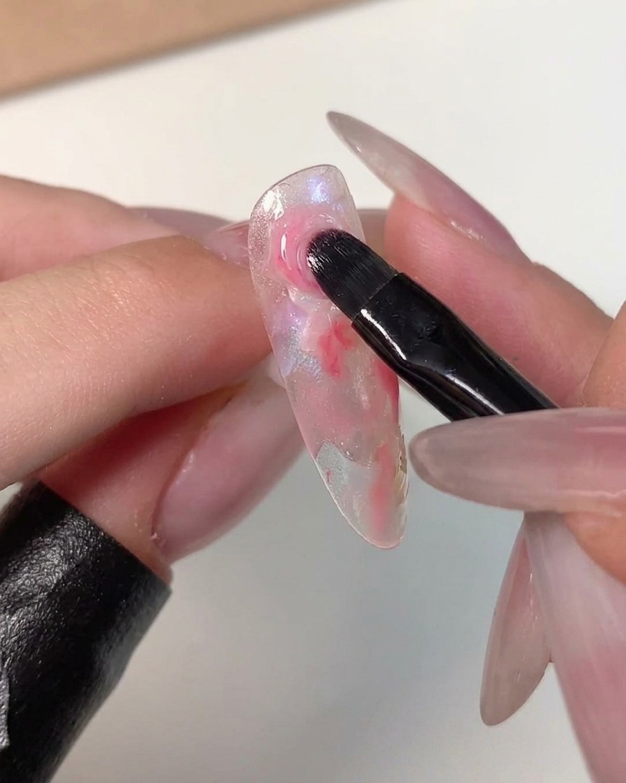 Un pinceau de nail art dégradant les contours dun point rose foncé dans les couleurs claires environnantes sur une capsule.