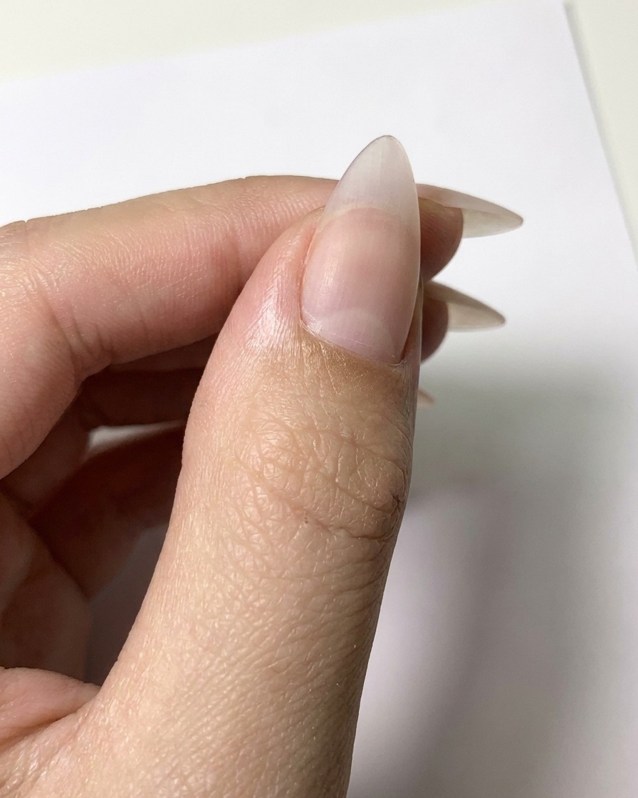 Un pinceau fin appliquant des contours en gel blanc sur une surface dongle nude mate pour former des formes de pétales.