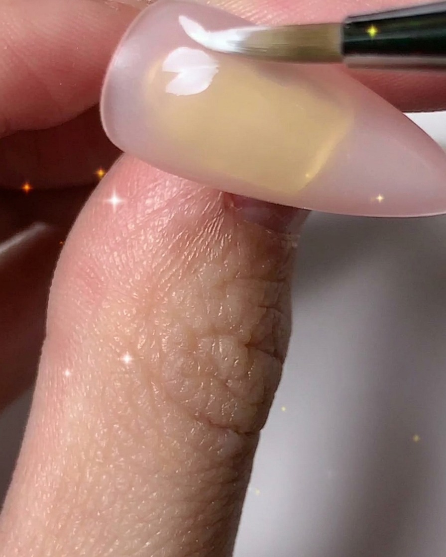 Un pinceau à ongles ajoutant des pétales blancs pour compléter plusieurs contours de fleurs sur la plaque de longle.
