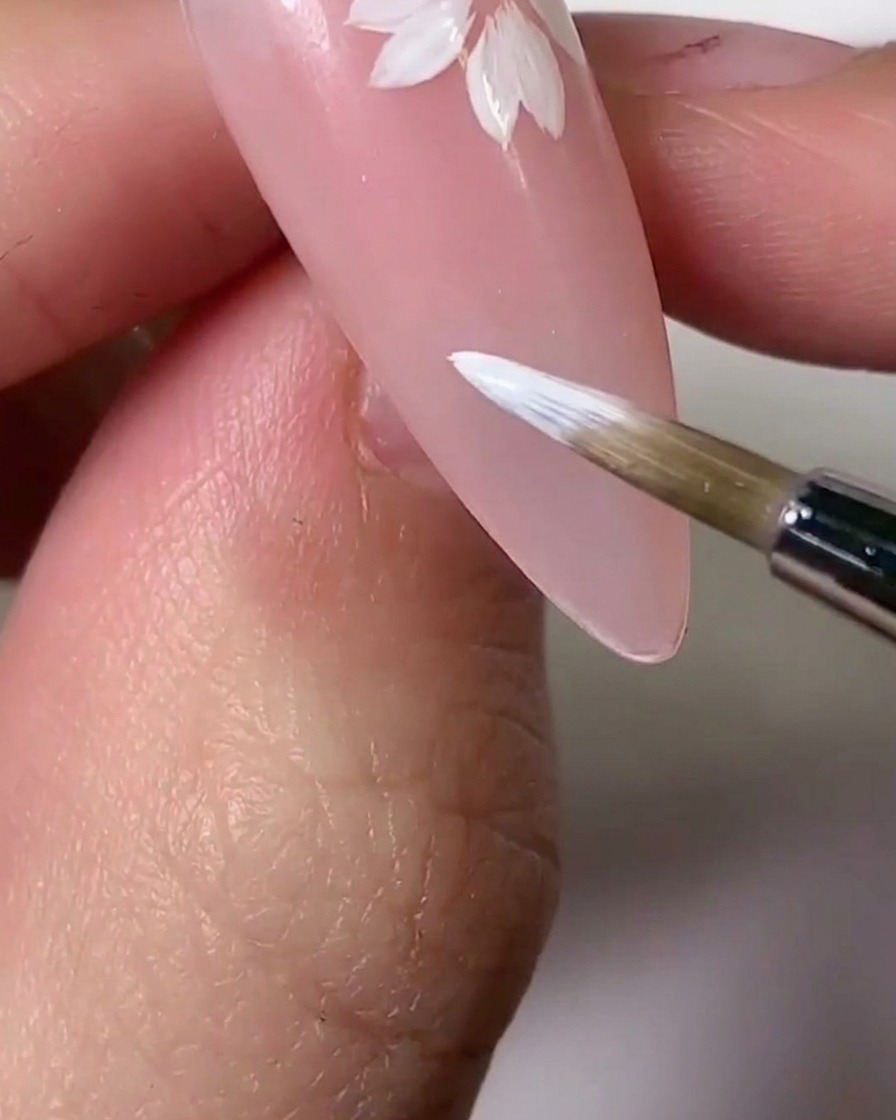 Un pinceau appliquant une teinte de gel rose clair sur des sections des pétales blancs pour un effet dégradé.