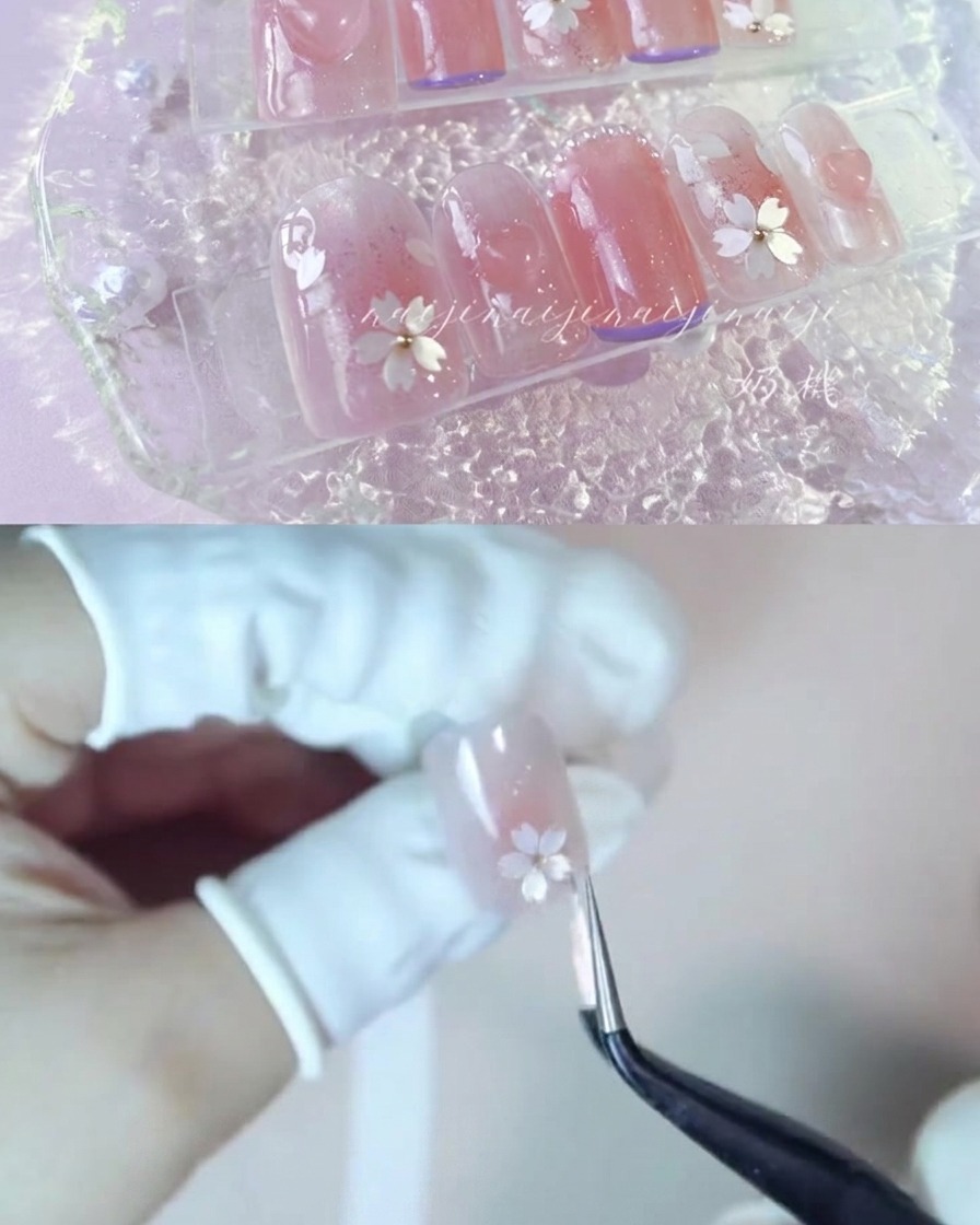 Une pince de précision plaçant soigneusement des fragments de pétales de fleurs de cerisier blanches sur un ongle brillant.