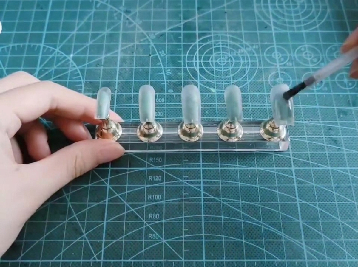Un pinceau appliquant une couche de gel cat-eye translucide sur une capsule dongle.