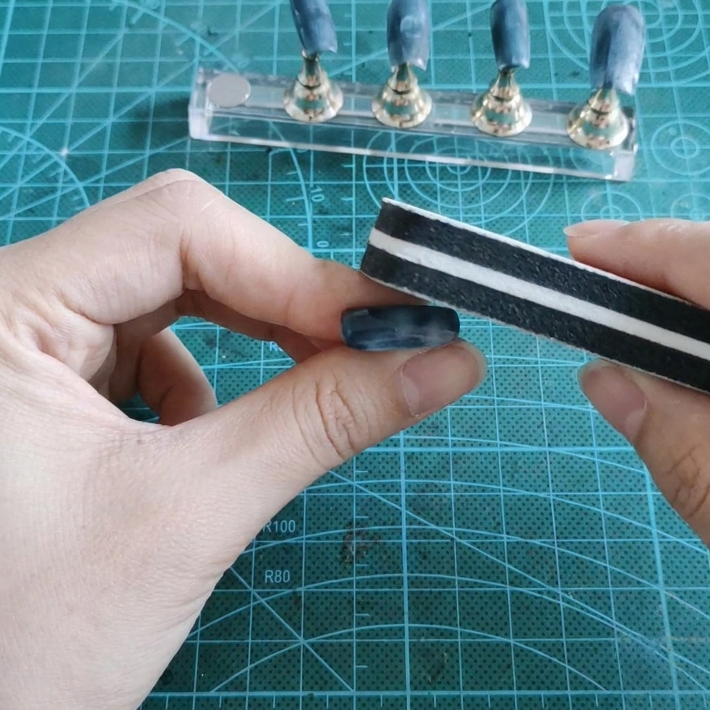 Un bloc polissoir ponçant la surface brillante en gel dun faux ongle tenu entre les doigts.