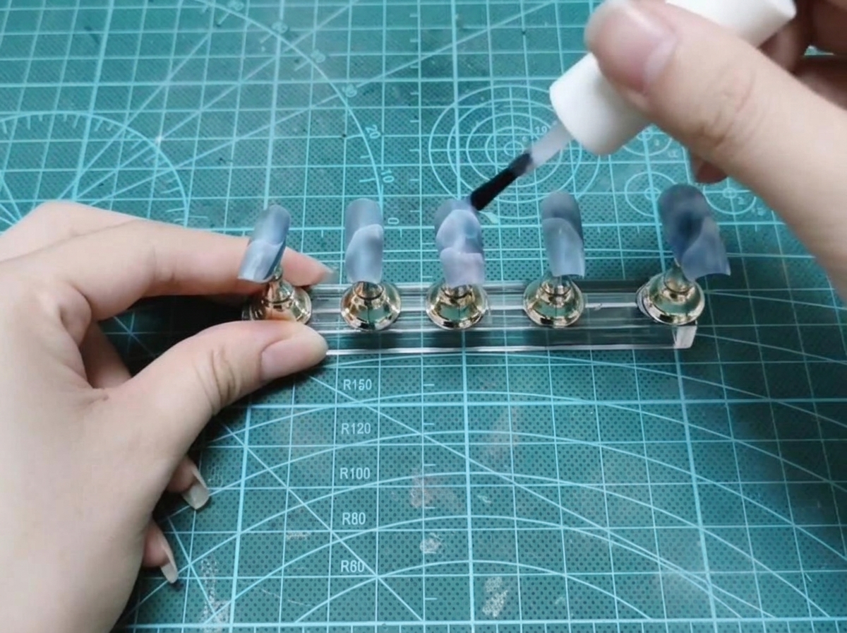 Un pinceau flacon appliquant du gel de construction transparent sur un ensemble de faux ongles peints.