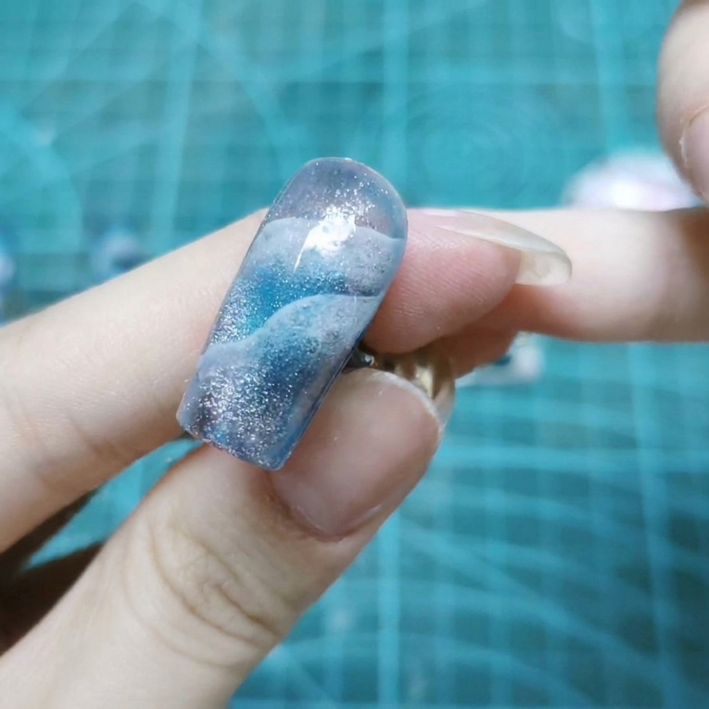 Gros plan sur un ongle recouvert de paillettes holographiques scintillantes incrustées dans du gel transparent.
