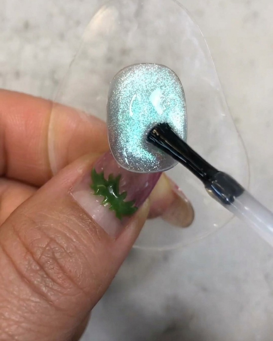 Un pinceau appliquant une petite goutte de gel de renfort transparent sur la surface texturée de longle bleu cat-eye.