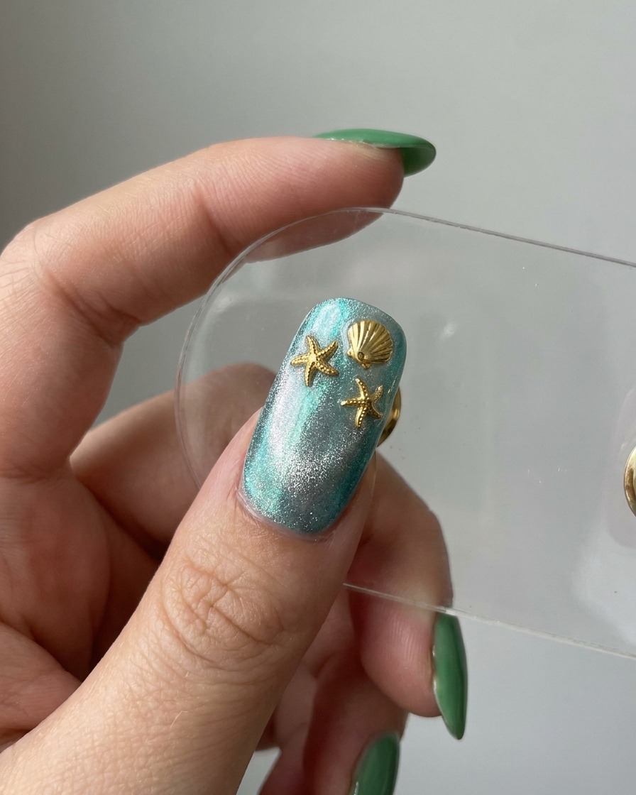 Un aperçu de longle terminé montrant une base cat-eye bleue décorée détoiles de mer et de breloques en forme de coquillage dorées.