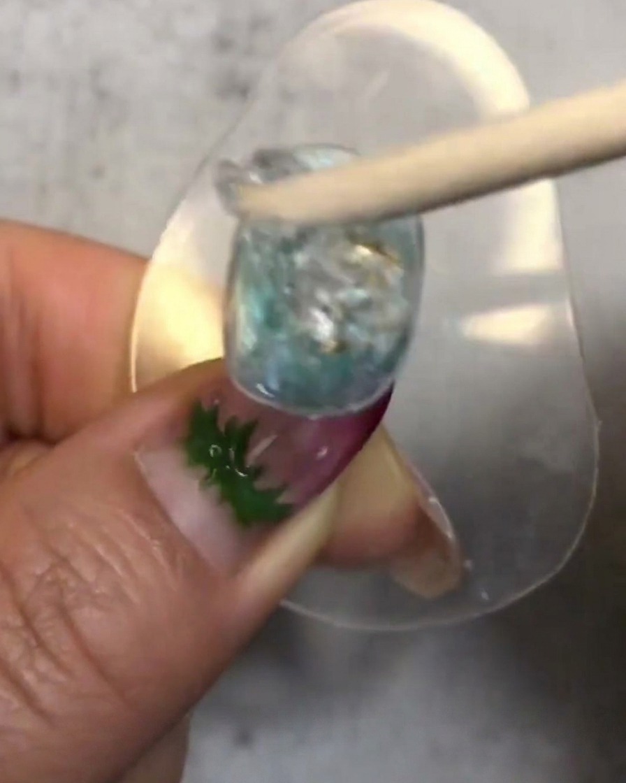 Un bâtonnet en bois mélangeant et plaquant une noisette de soft candy gel translucide sur longle décoré.