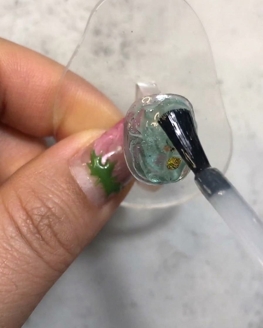 Un pinceau à ongles appliquant un top coat transparent sur un ongle en gel translucide texturé.
