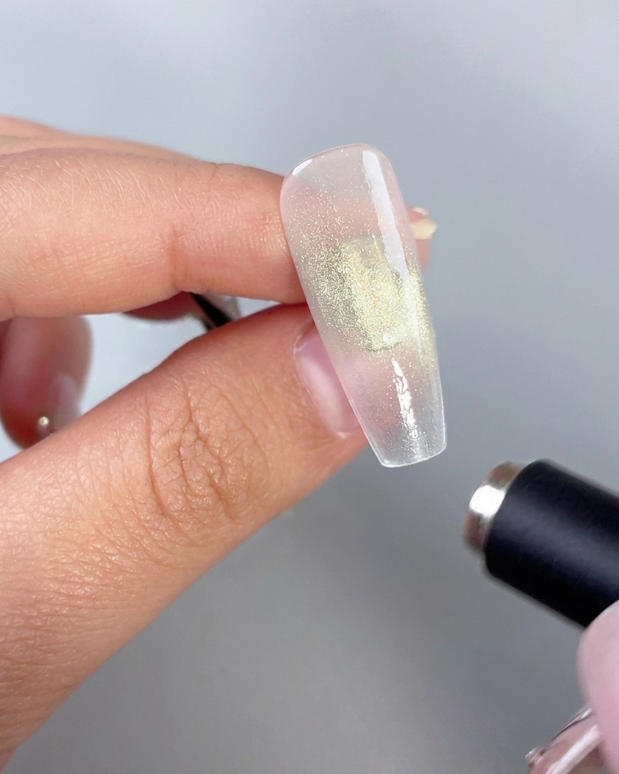 Un baton aimanté cylindrique tenu près dun ongle en gel vert brillant pour activer leffet œil-de-chat.