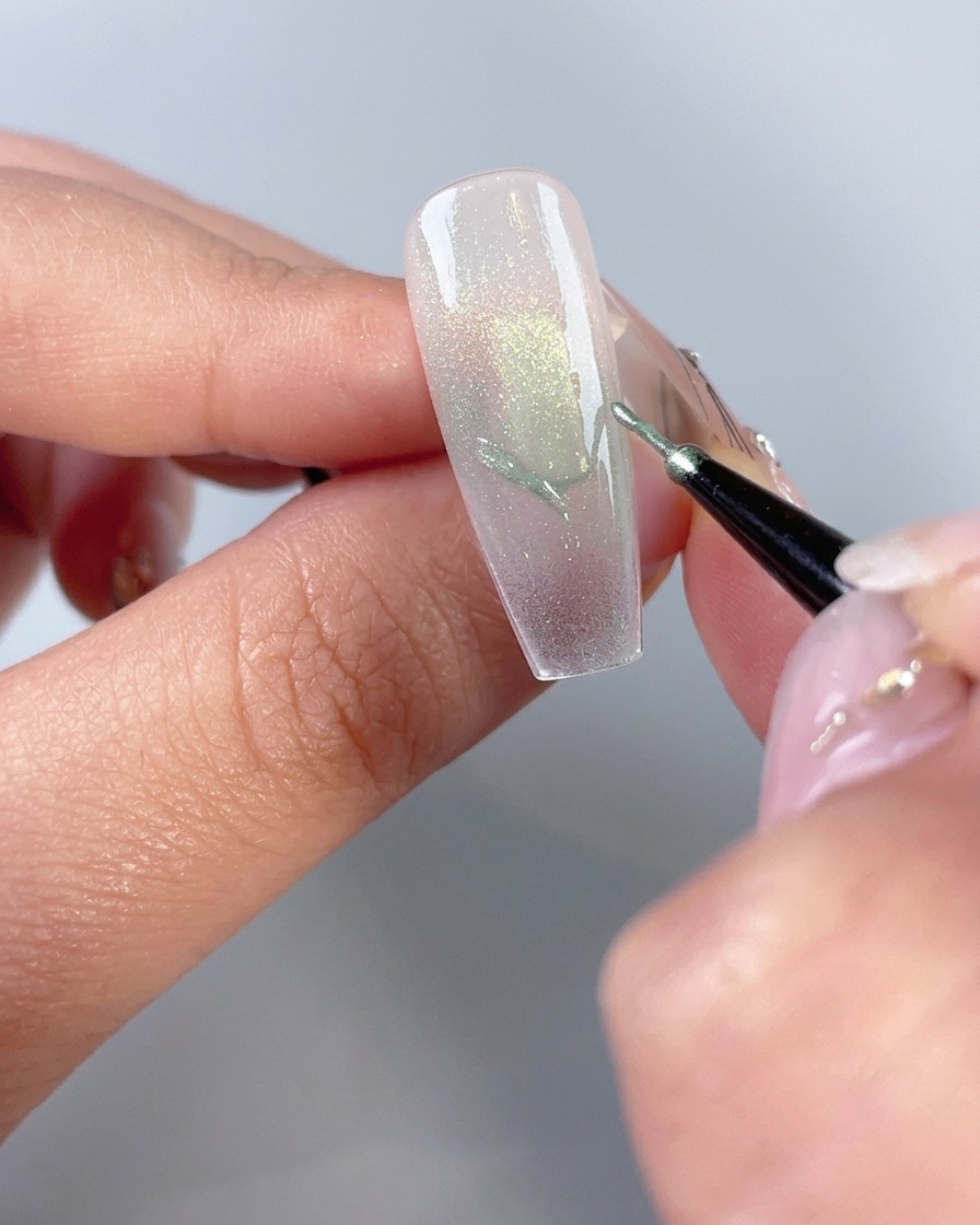 Un pinceau fin pour nail art dessinant les contours dailes de papillon sur une capsule dongle manucurée.