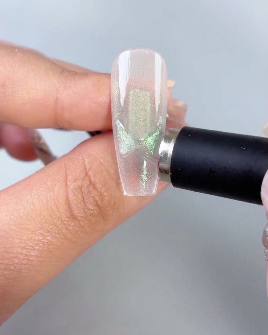 Un bâton aimanté noir tenu près du côté dune capsule dongle transparente mettant en valeur des motifs dailes de papillon verts activés.