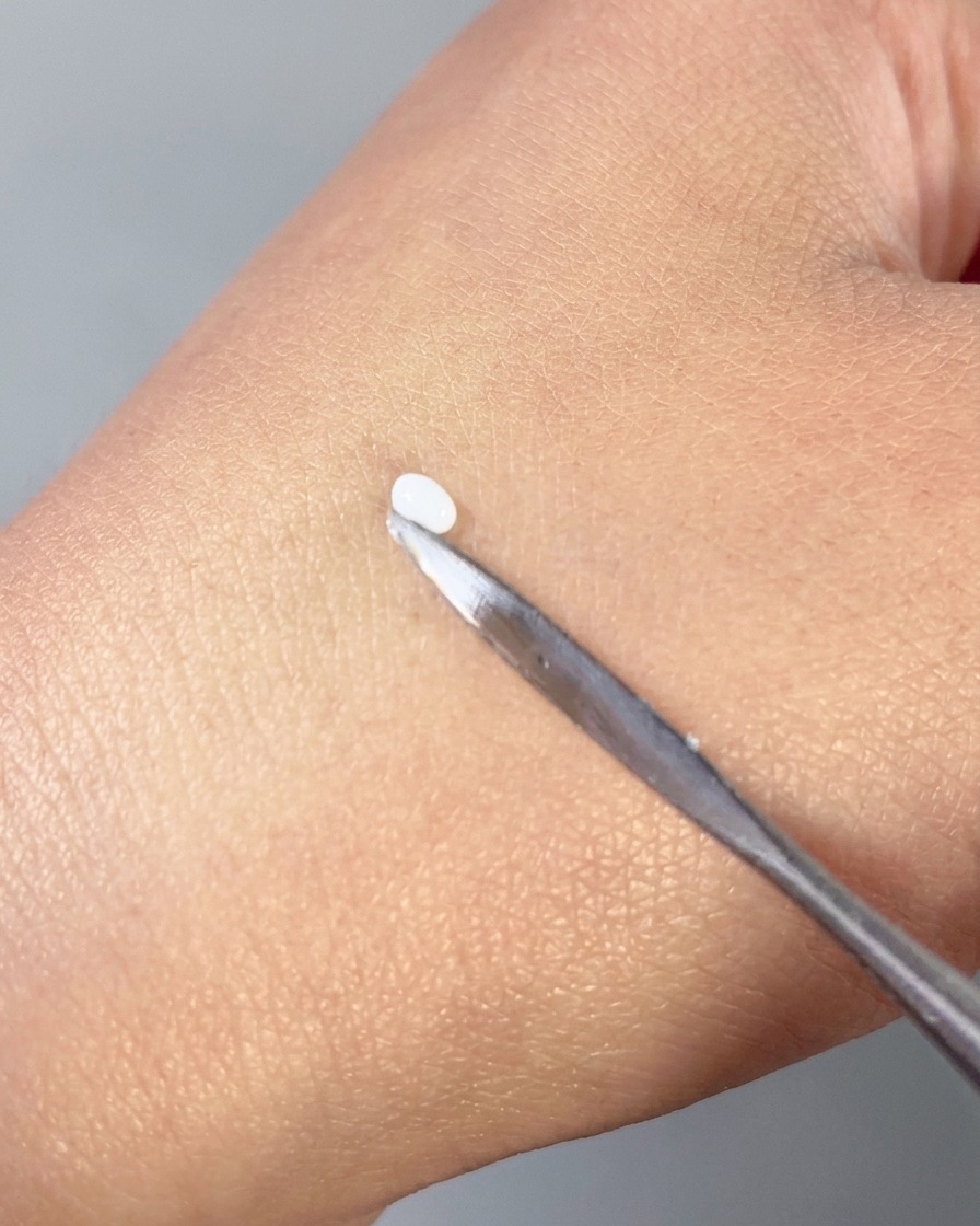 Une spatule métallique pressant une petite perle blanche de gel 3D pour lui donner une forme de pétale lisse sur le dos dune main.