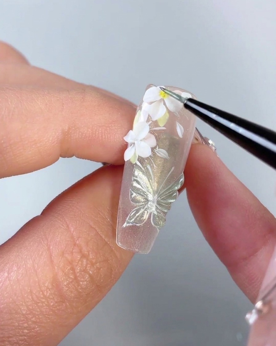 Un pinceau fin ajoutant un minuscule point jaune au centre dune fleur blanche 3D sur un ongle.