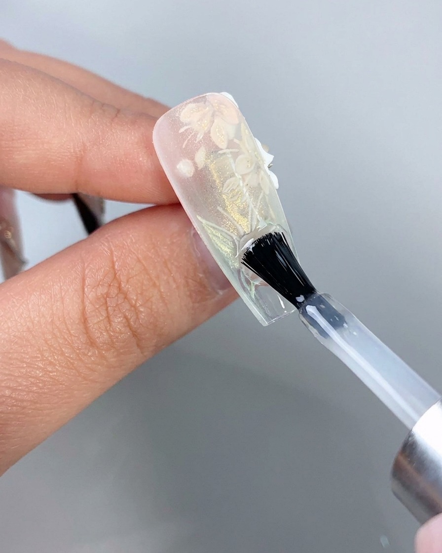 Un pinceau à ongle appliquant une couche de finition transparente sur le dessous du bord libre dune capsule dongle rallongée.