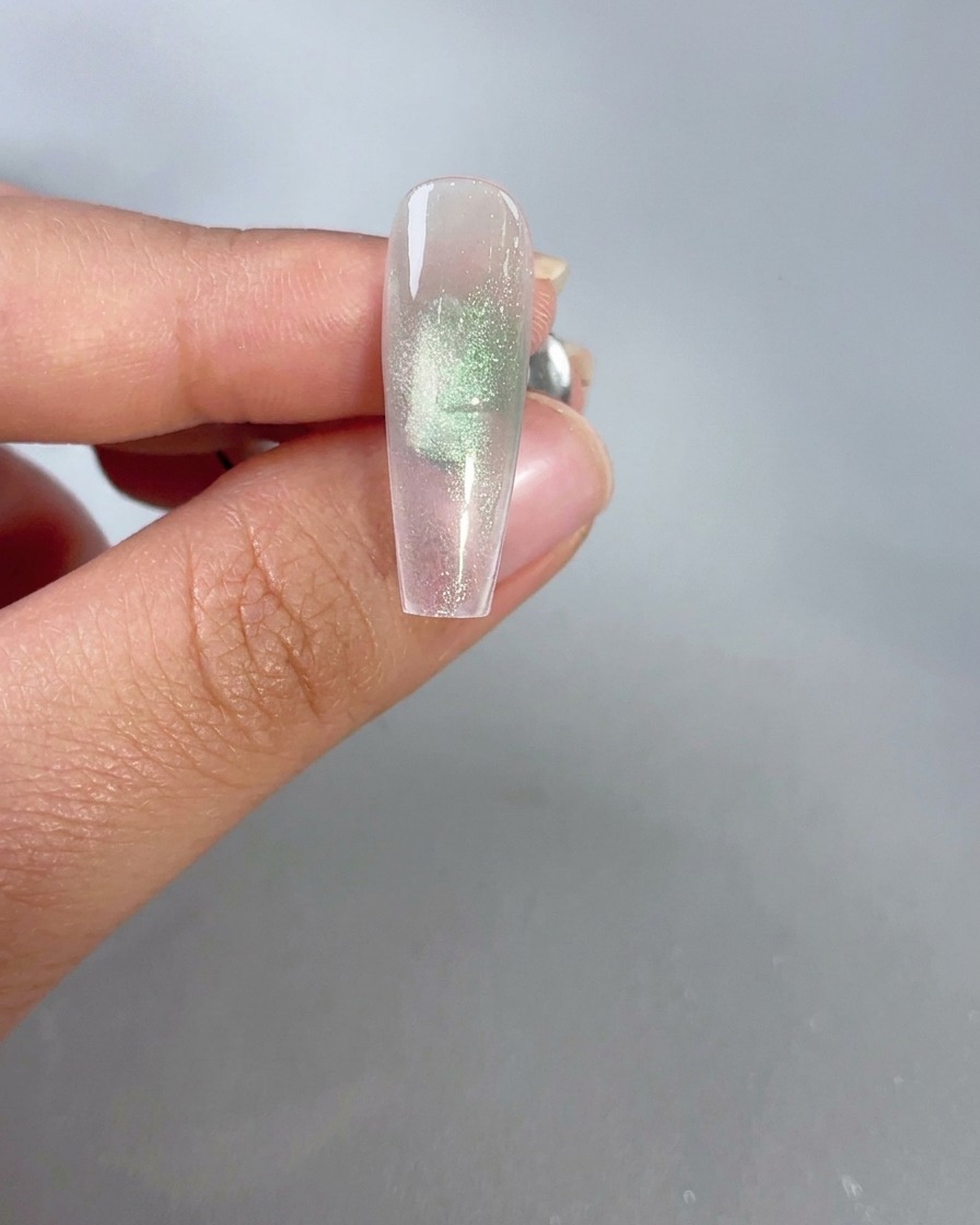 Un aimant tenu près dun ongle en gel œil-de-chat vert diaphane pour activer leffet scintillant.