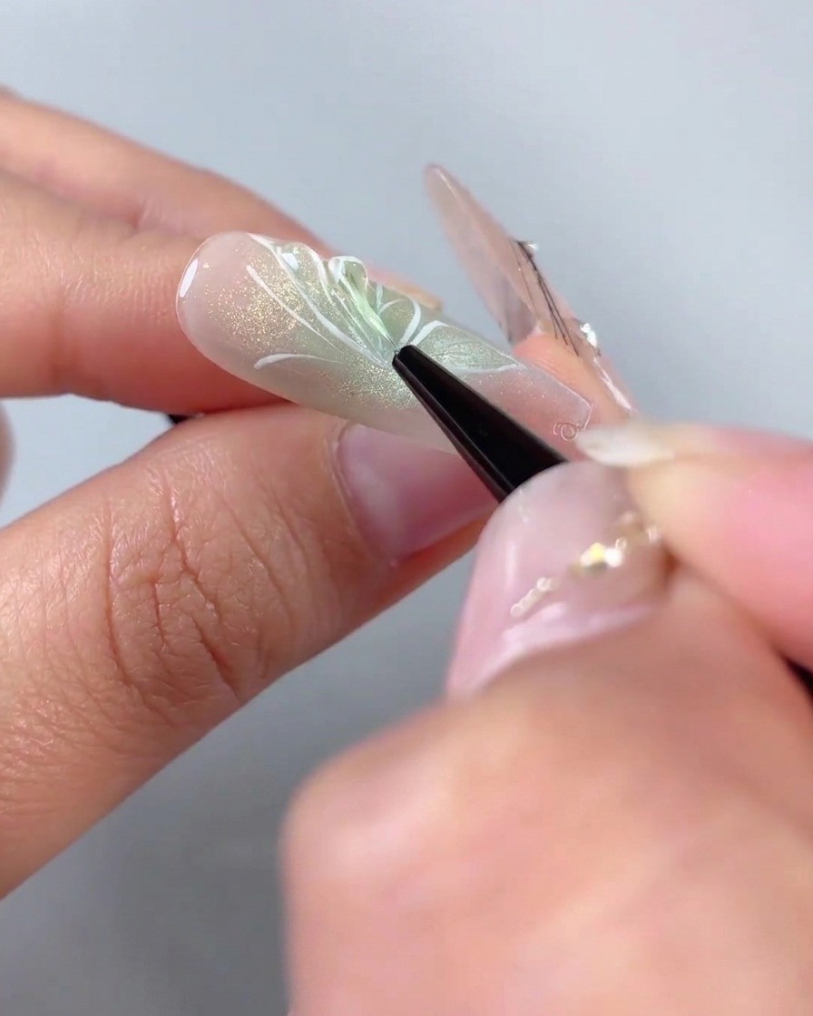 Un pinceau traceur fin appliquant du gel de modelage 3D transparent sur les contours dailes peints en blanc dun design dongle demi-papillon.