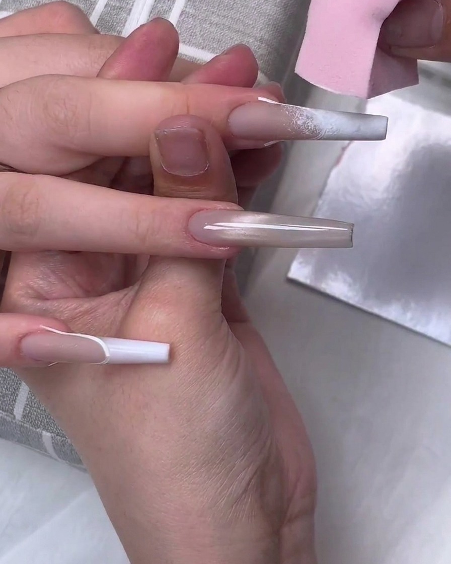 Une éponge de maquillage rose tamponnant du vernis gel blanc sur le bout dun long ongle en forme de cercueil pour créer un effet dégradé.