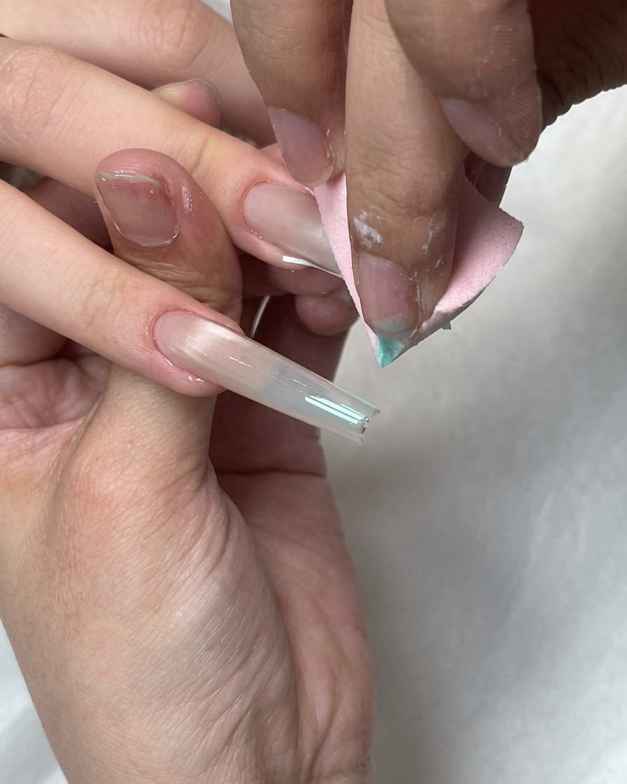 Une éponge de maquillage rose estompant des points de gel bleu sur le bout French blanc dun long ongle.