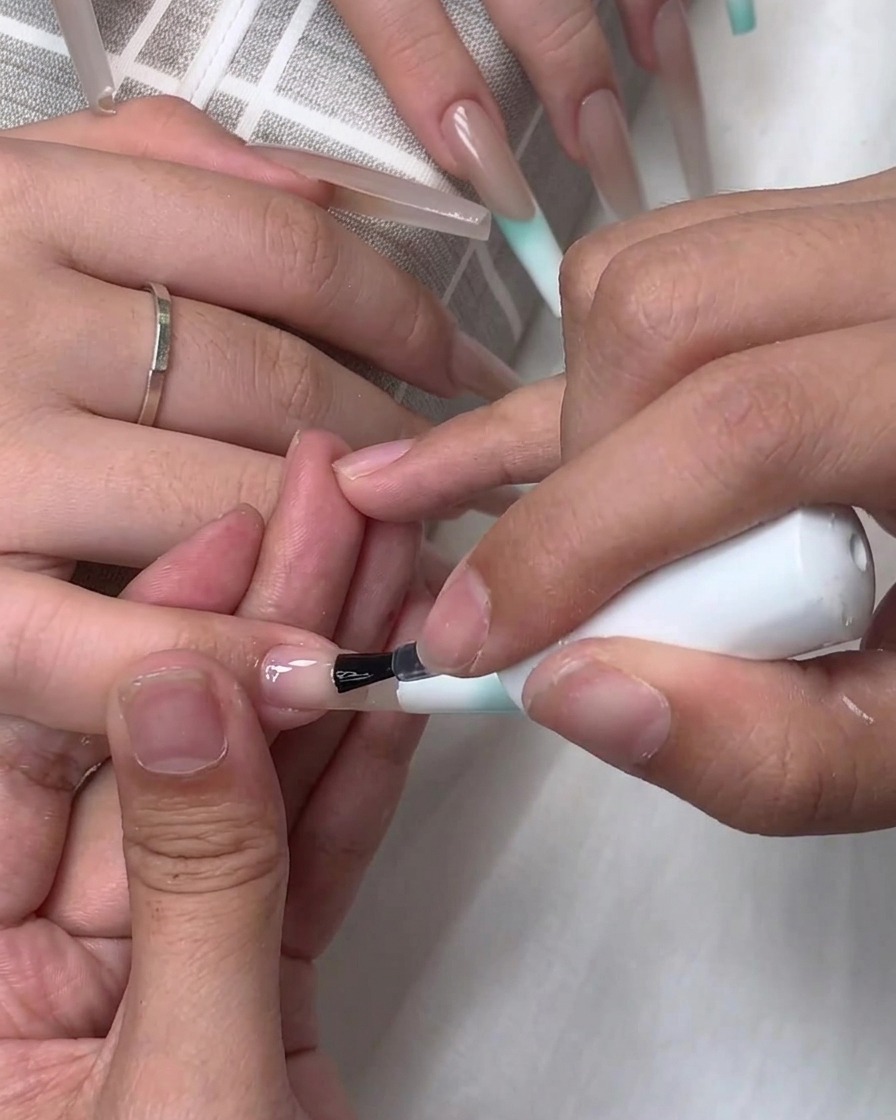 Un pinceau appliquant du gel de base transparent ou du top coat sur la surface dun ongle rallongé.