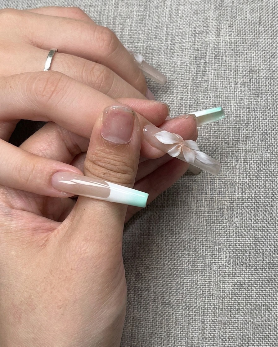 Un petit effet de dégradé rose créé au centre dune fleur sculptée en 3D blanche sur un ongle.
