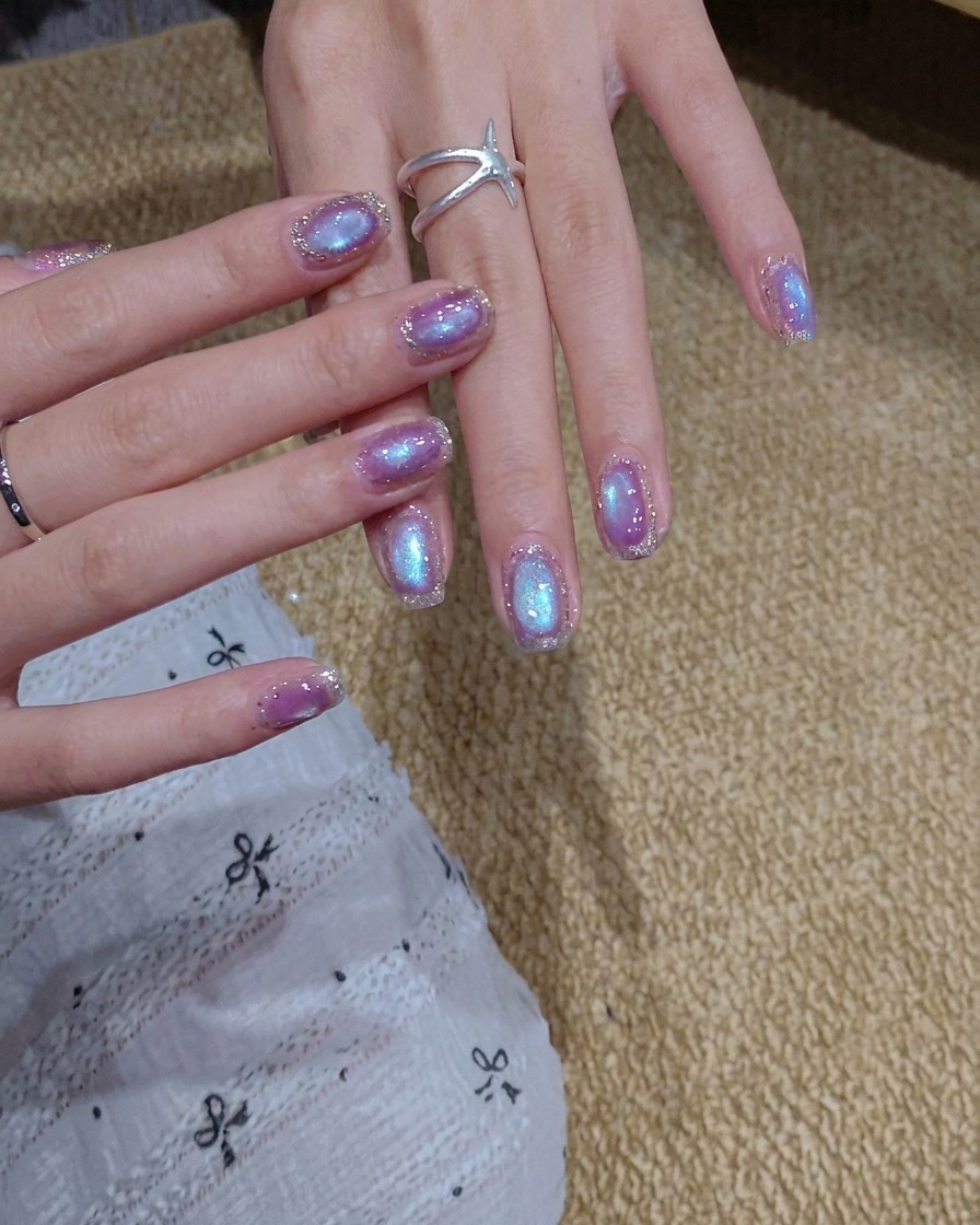Un pinceau appliquant une couche de vernis gel cat eye bleu-violet scintillant sur un ongle.