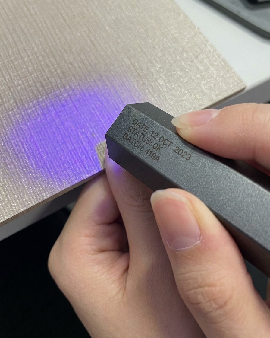 Une main plaçant un pouce sous une mini lampe UV LED portable grise compacte.