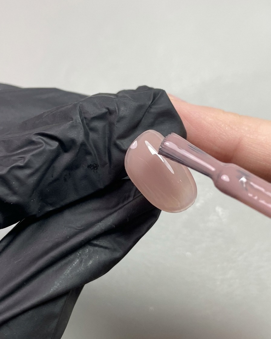 Un pinceau appliquant une seconde couche de gel nude transparent aux notes orangées sur un onglet.