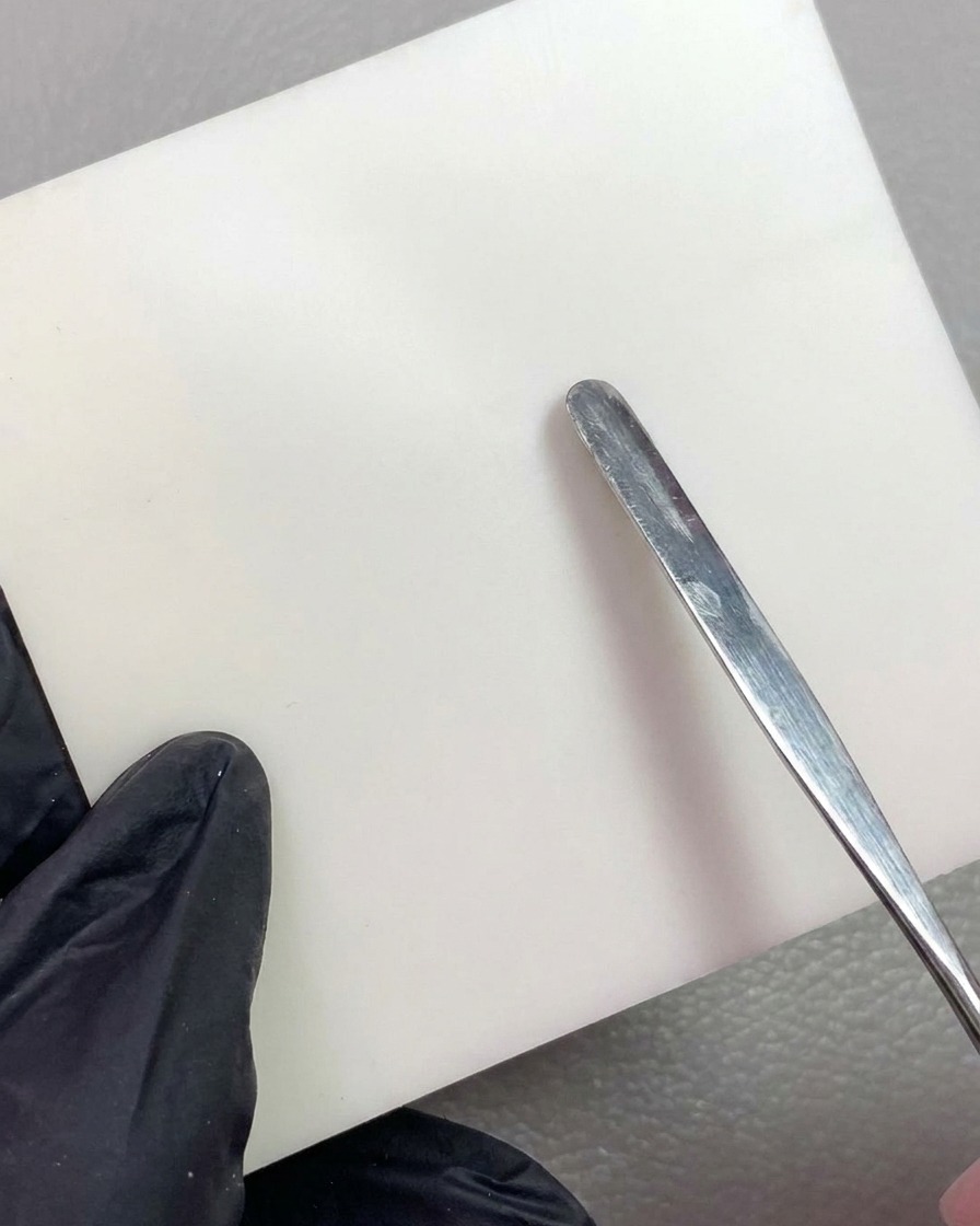 Un outil en métal déposant un morceau de gel de modelage blanc sur une palette de mélange propre.