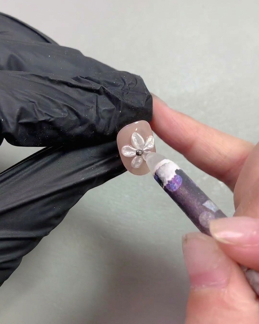Un outil de type stylo de cire plaçant de minuscules billes dacier métalliques au centre dun nail art de fleur nacrée.