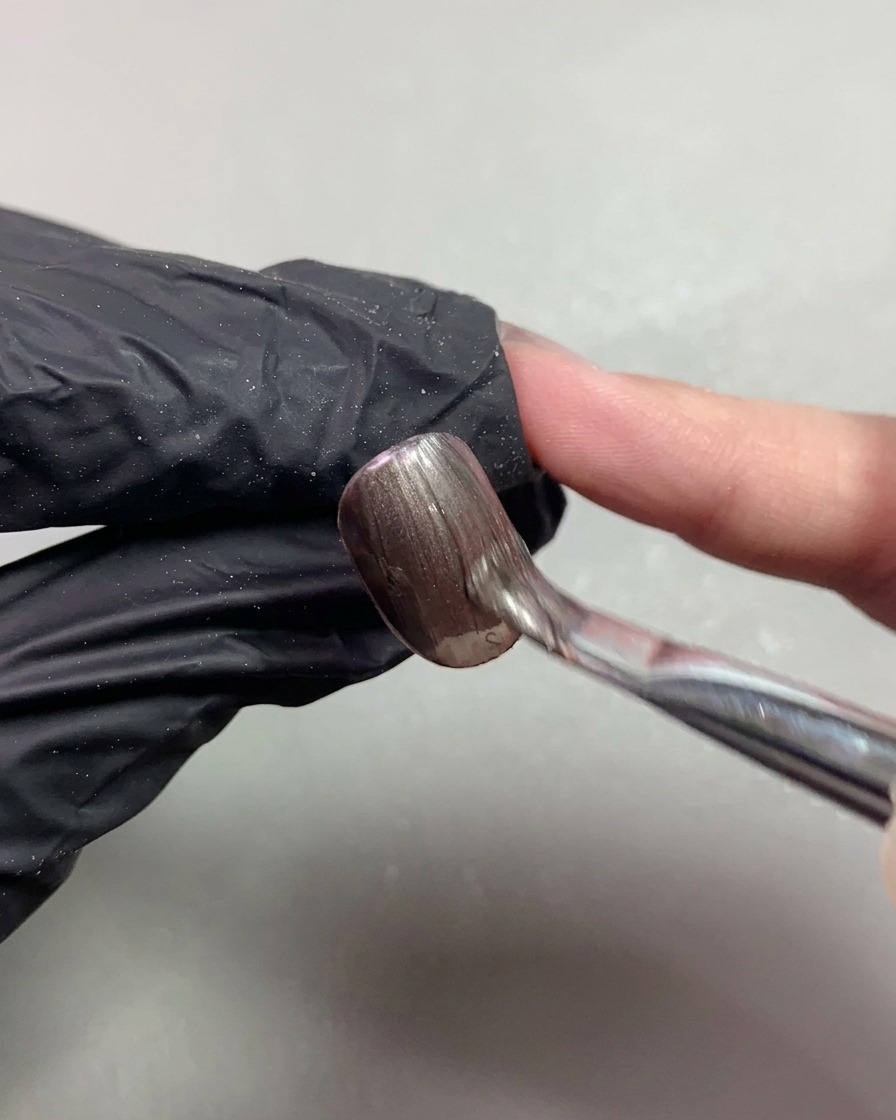 Un pinceau appliquant du gel cat-eye magnétique marron foncé en douceur sur un ongle court.
