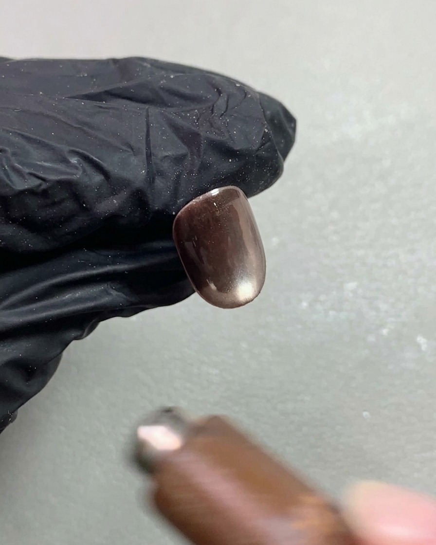 Un aimant à ongles survolant un ongle court en gel cat-eye marron foncé, façonnant le pigment réfléchissant en un effet de sphère lumineuse et mouvante.
