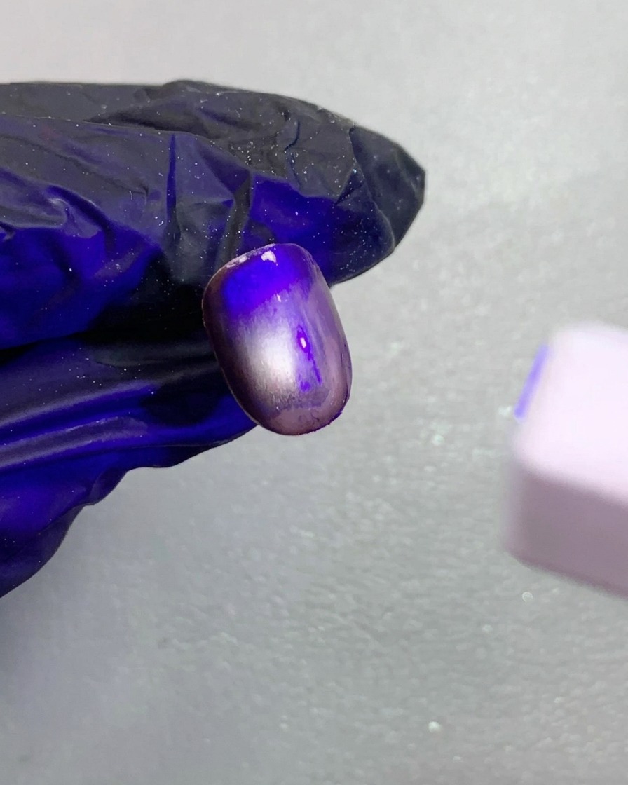 Vue rapprochée dun ongle cat-eye magnétique marron foncé en cours de catalyse sous une petite lampe UV.