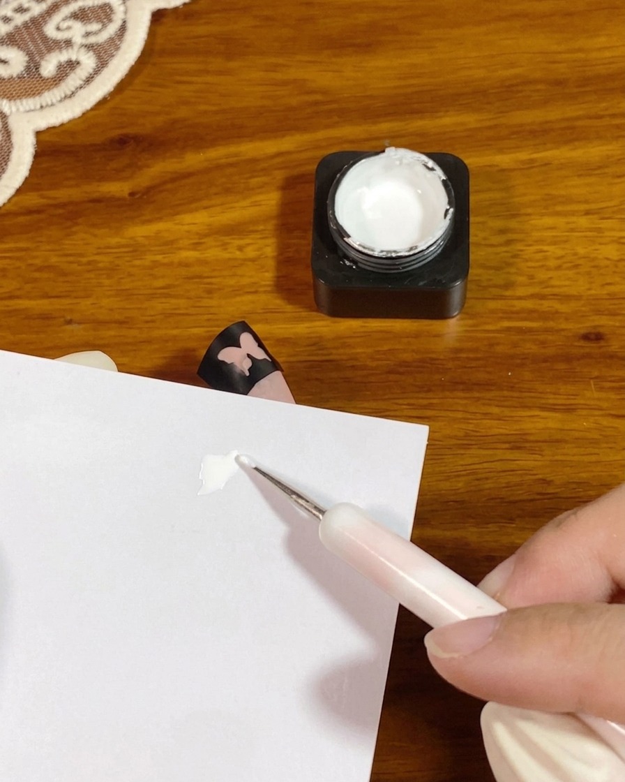 Un outil de dotting plaquant une petite noisette de gel de tapotage blanc épais sur un papier palette blanc.