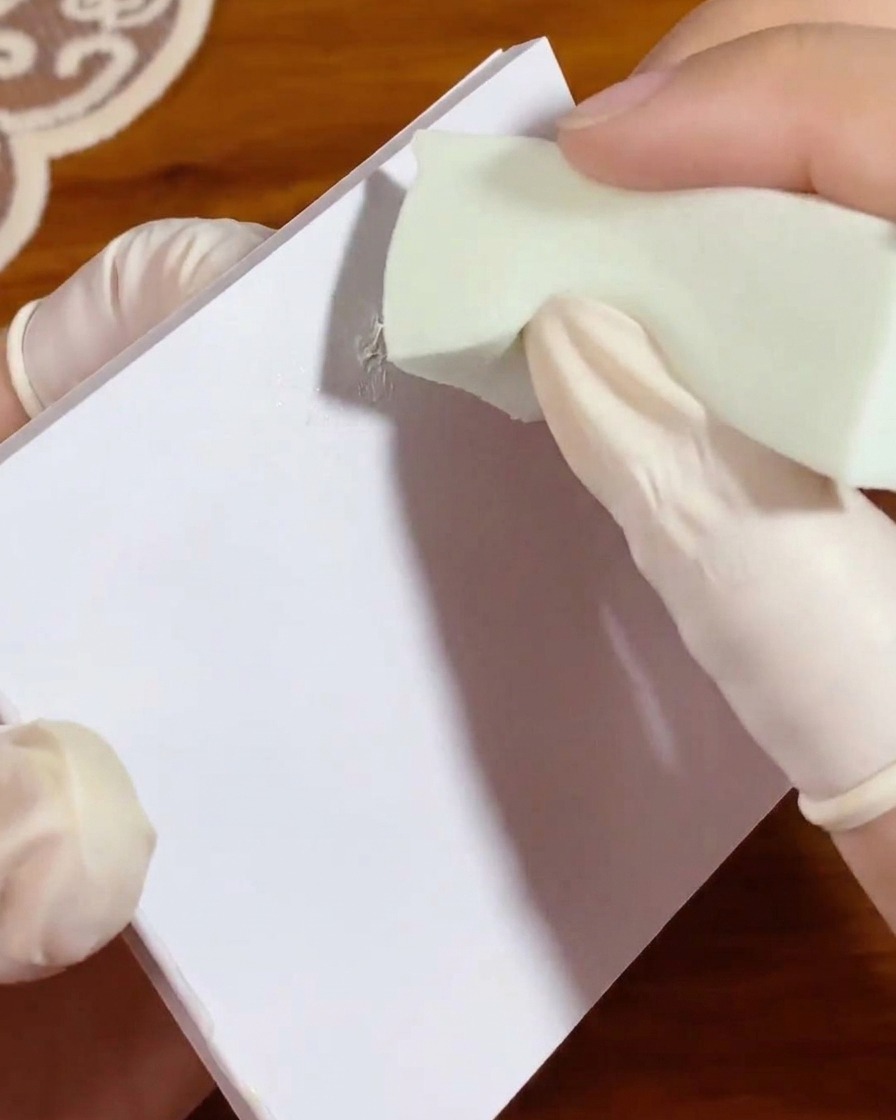 Une petite éponge de maquillage verte tamponnée dans une touche de gel blanc sur un papier palette pour répartir uniformément la couleur.
