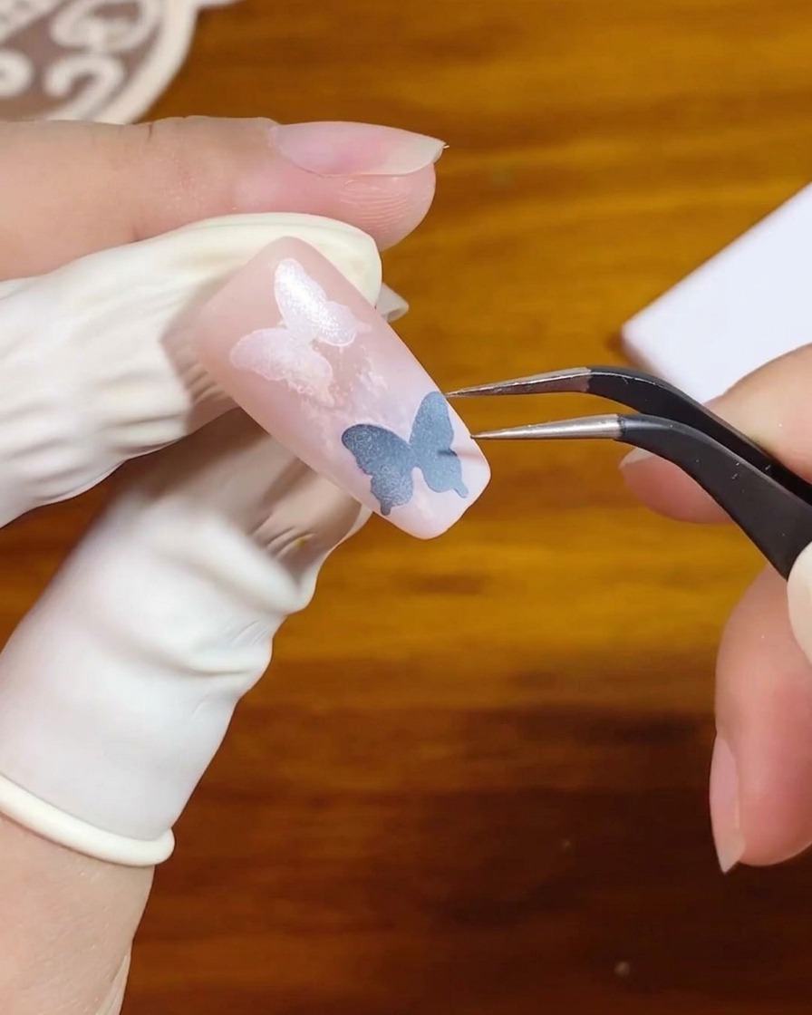 Une paire de pinces soulevant un autocollant pochoir dun design dongle en dégradé rose.