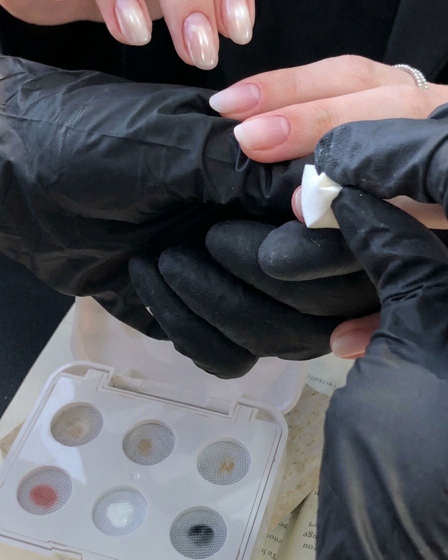 Main gantée utilisant un outil de tampon éponge blanc pour appliquer un dégradé blanc ivoire sur un onglet près de la cuticule.