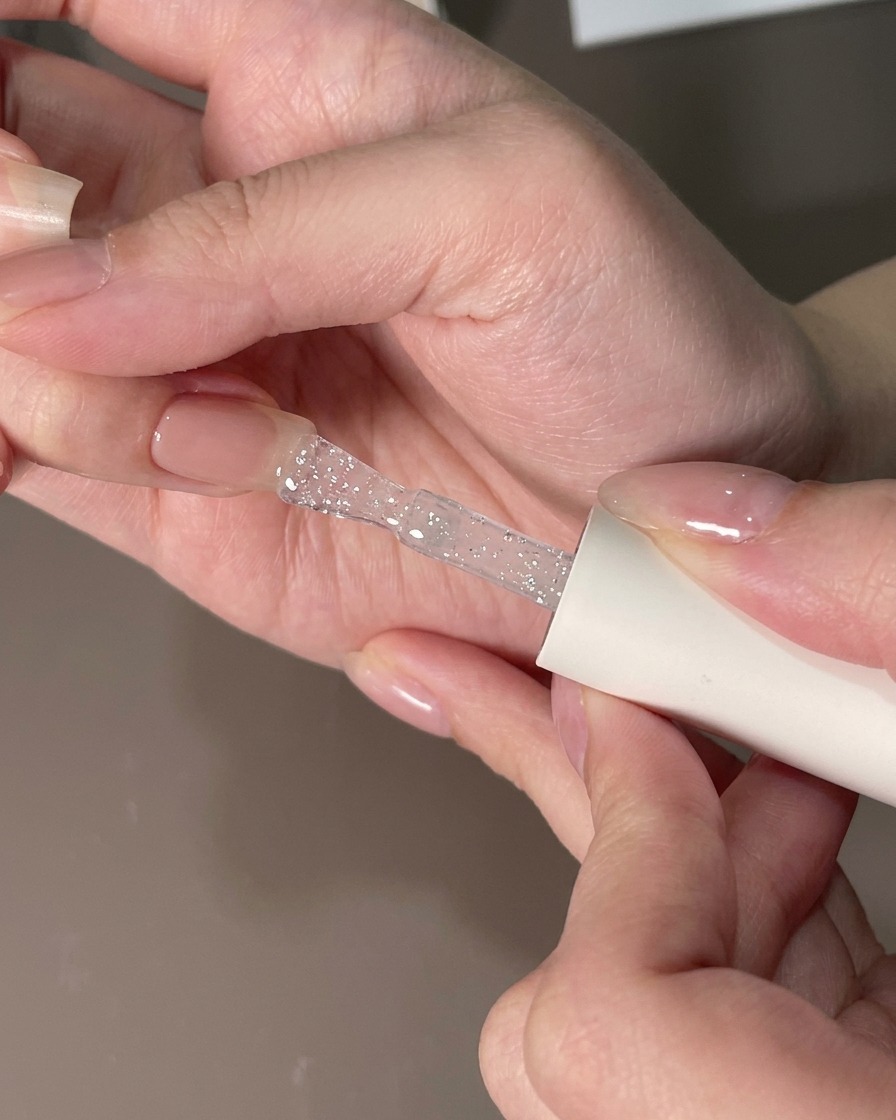 Un pinceau plat lissant une couche de gel transparent sur un ongle pour éliminer les particules.