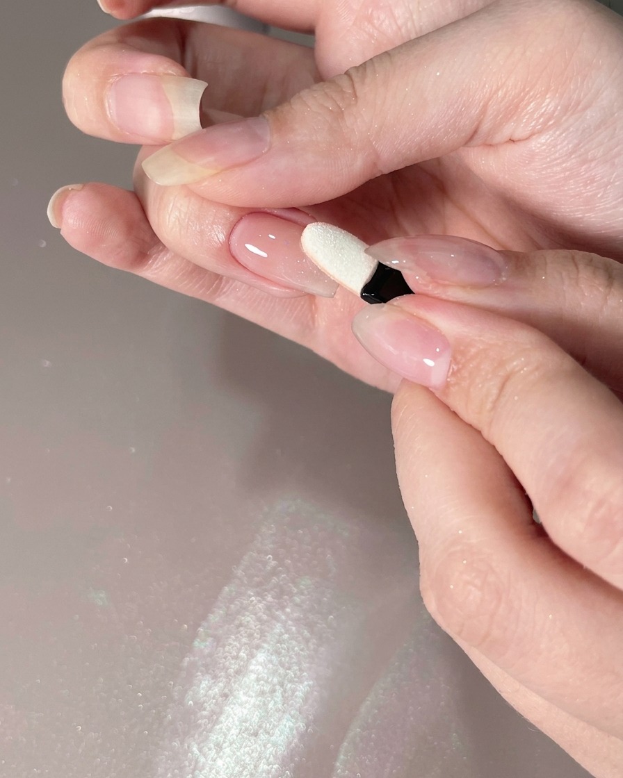 Un applicateur en mousse déposant de la poudre chrome sur le bord dun ongle.