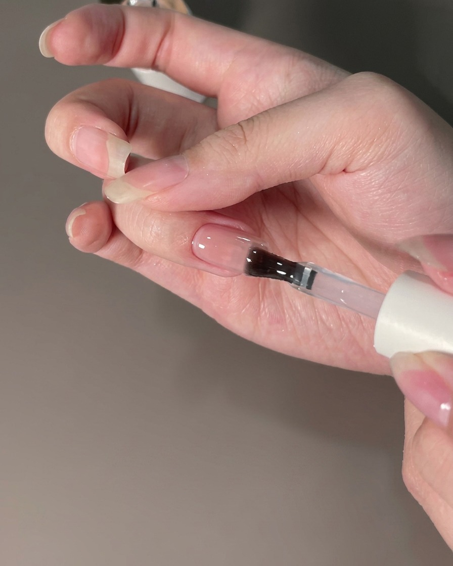 Un pinceau appliquant un top coat scellant sur un ongle doté dune finition en poudre chrome.