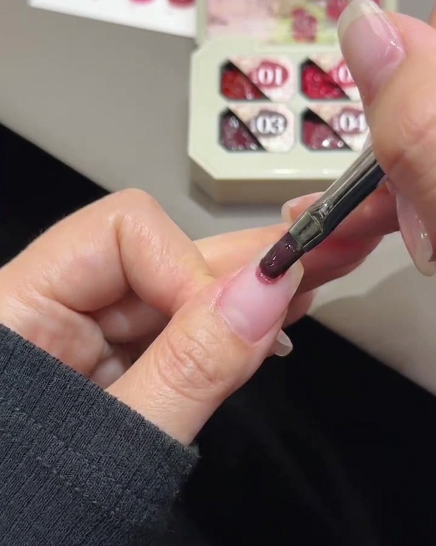 Un pinceau à ongles appliquant du gel rose par touches sur le bout dun ongle naturel.